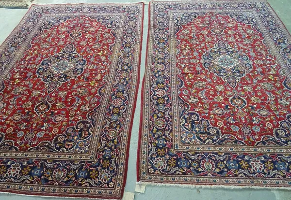 A pair of Kashan rugs, Persian, each with a dark madder field centred by an indigo medallion matching spandrels, all with floral sprays; a dark indigo