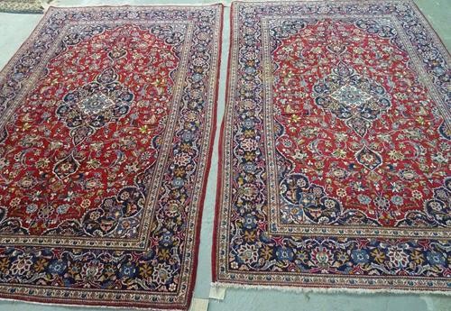 A pair of Kashan rugs, Persian, each with a dark madder field centred by an indigo medallion matching spandrels, all with floral sprays; a dark indigo