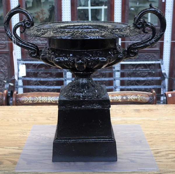 A black painted cast iron twin handle urn, on square stand, 63cm wide x 61cm high.