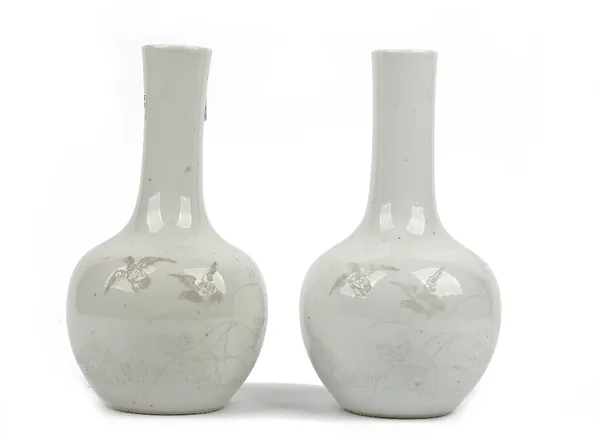 A pair of Chinese white-glazed bottle vases, late 19th/20th century, each painted in grey monochrome with two birds in flight above lotus, the reverse