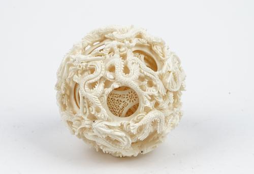 A large Canton ivory puzzle ball, early 20th century, the outer ball carved and pierced with dragons amongst cloud scrolls, containing around five con