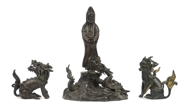 Two Chinese bronze Buddhistic lions, 19th century, 7.5cm high, and a Chinese bronze figure of Guanyin, standing above a dragon, on a wavy base, 20cm h