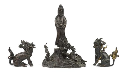 Two Chinese bronze Buddhistic lions, 19th century, 7.5cm high, and a Chinese bronze figure of Guanyin, standing above a dragon, on a wavy base, 20cm h