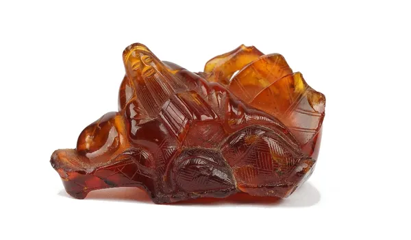 A Chinese amber brush holder or water pot, Qing dynasty, in the form of a sage with a book leaning against a large fruit, incised characters, 8cm wide