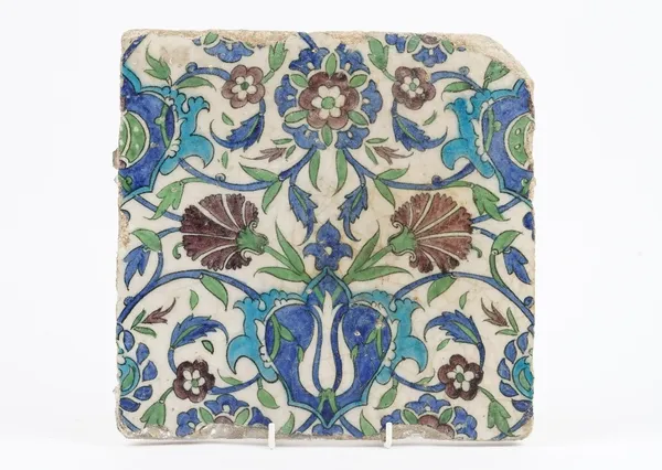 A large Iznik pottery tile, probably 18th century, painted in green, blue and aubergine with carnations and other flowers, 27cm square.