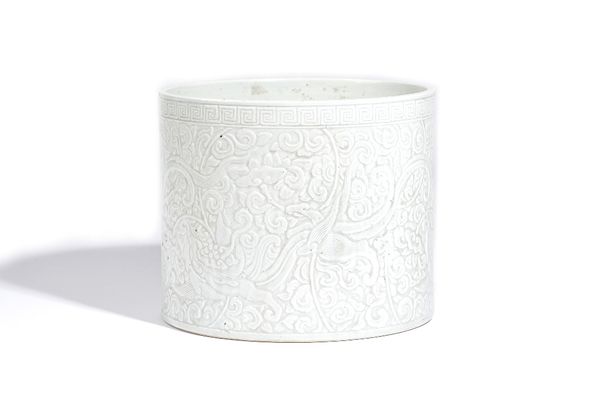 A Chinese white glazed large brush pot, 19th/20th century, the sides carved with phoenix and mythical beasts amongst lotus beneath a key pattern borde