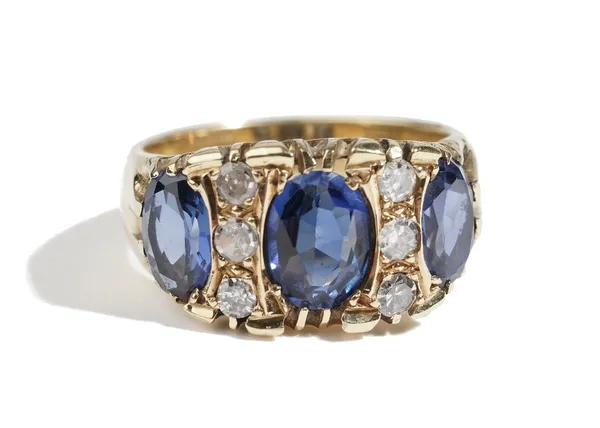 A gold, synthetic sapphire and diamond ring, mounted with three oval cut synthetic sapphires and with two rows of three circular cut diamonds, detaile