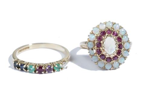 A 9ct gold, opal and ruby oval cluster ring, claw set with an oval opal to the centre, in a surround of circular cut rubies, with an outer border of c