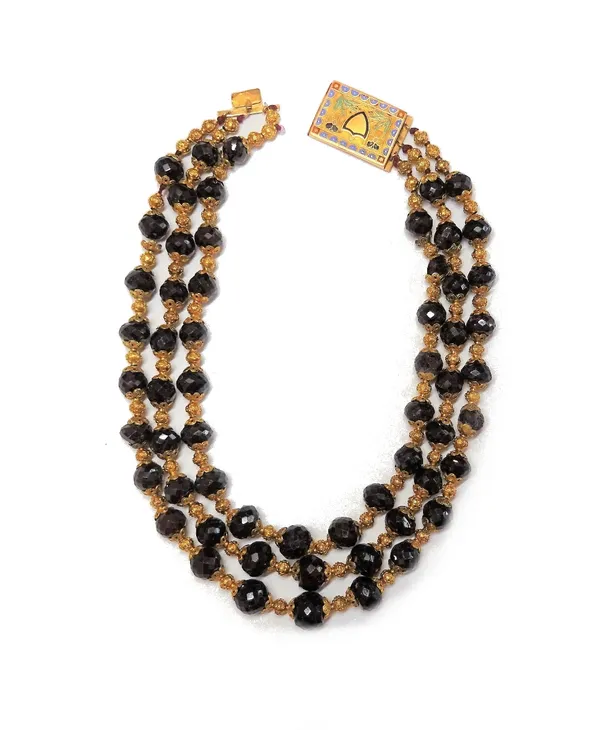 A three row necklace of graduated faceted garnet beads, with gold decorated beads spaced at intervals, on a gold and enamelled rectangular clasp, deco