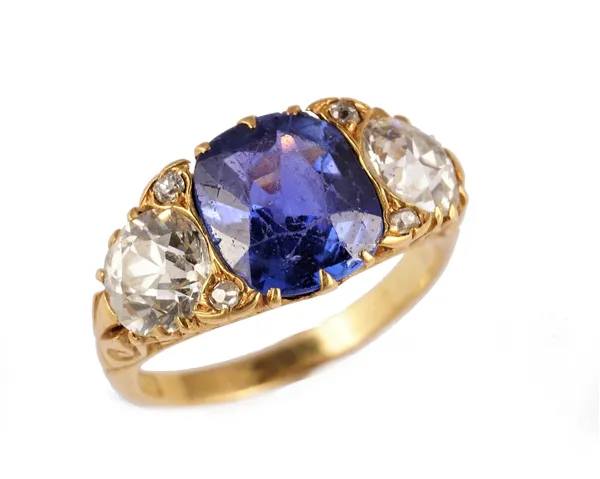 A gold, Ceylon sapphire and diamond ring, claw set with the cushion shaped Ceylon sapphire at the centre, between two principal cushion shaped diamond