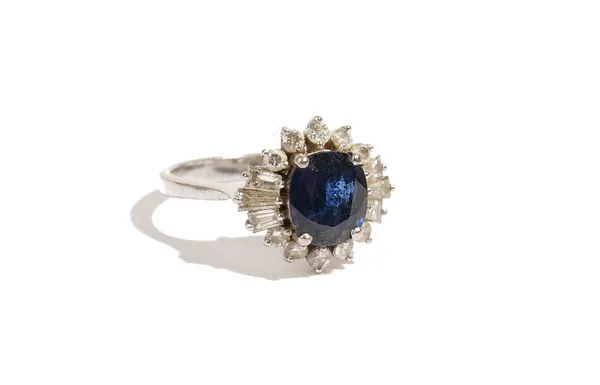 A 14ct white gold, sapphire and diamond-set ring of cluster design, the oval-cut sapphire approximately 2ct, claw-set in a surround of circular and ta