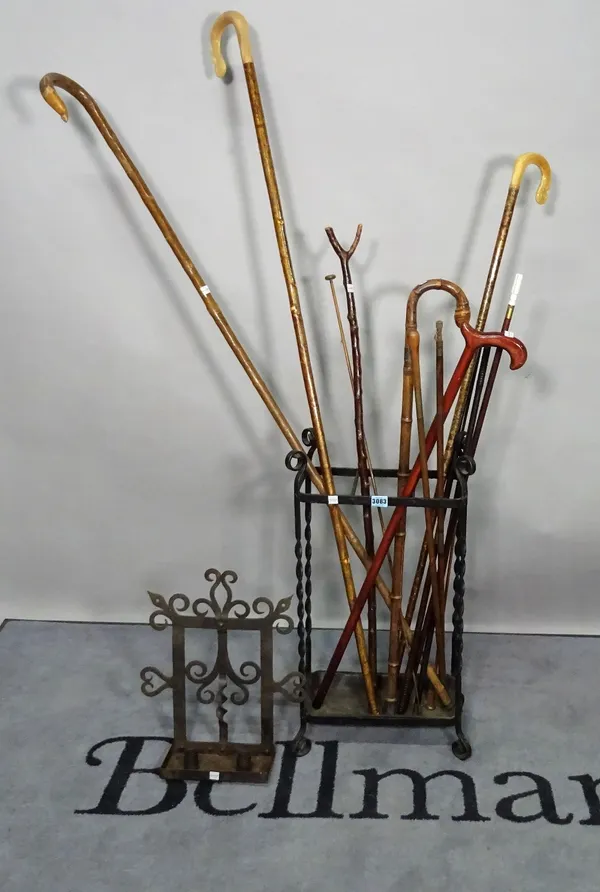 Six various canes in a wrought-iron stick stand, 38cm wide x 76cm high, and a wrought-iron twin-light candle stand, 36cm wide.