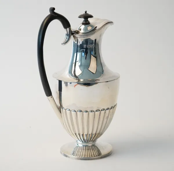 A silver hot water jug, of Adam style with partly fluted decoration and black fittings to the hinged lid and to the handle, raised on a circular foot,