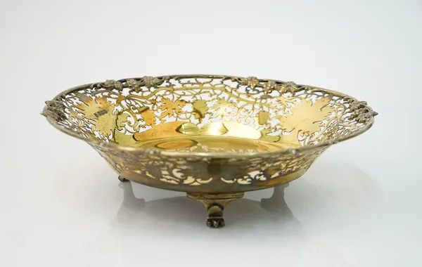 A silver gilt dish, of shaped circular form, cast and pierced with a border of fruiting vine, presentation inscribed to the centre, raised on three fe