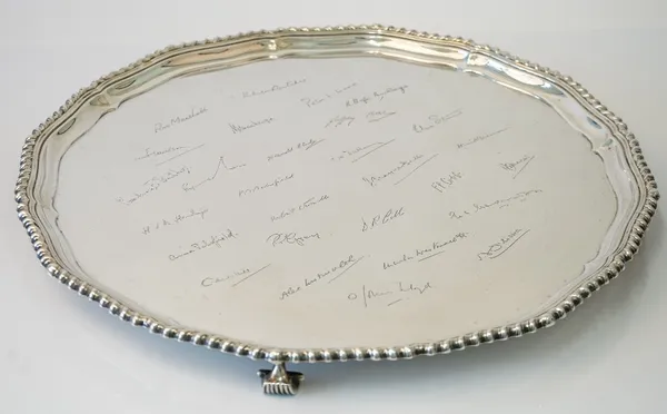 A large silver salver, of shaped circular form, having a pie-crust rim within a gadrooned border, in the Chippendale style, raised on four scrolled fe
