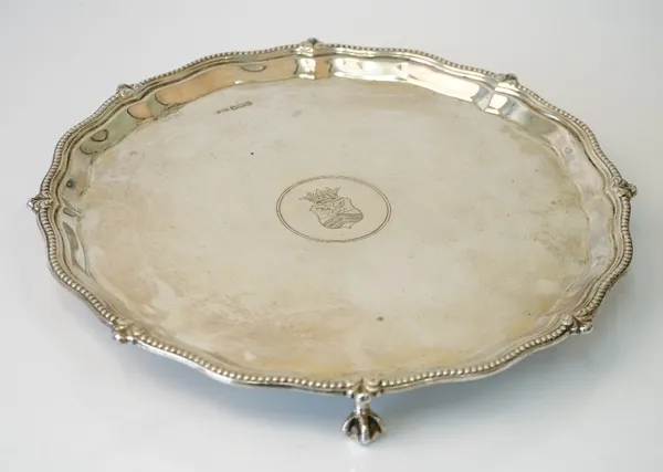 A silver shaped circular salver, engraved with a shield to the centre, decorated with a beaded rim, raised on three ball and claw feet, diameter 26cm,