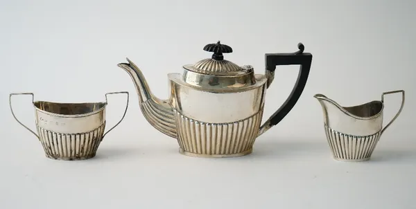 A late Victorian silver composite three piece tea set, comprising; a teapot with black fittings, Chester 1899, a twin handled sugar bowl, Birmingham 1
