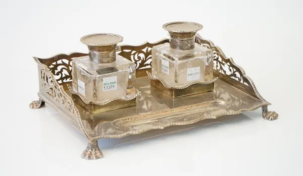 A silver twin bottle ink stand, of shaped rectangular form with pierced gallery sides below gadrooned rims, the front with a pen recess, raised on fou
