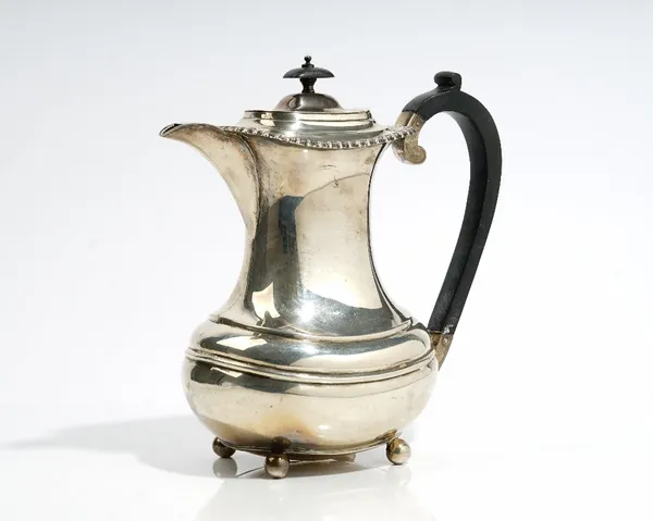 A silver hot water jug of waisted form, decorated with a gadrooned rim, raised on four spherical feet and having black fittings, Sheffield 1925, gross