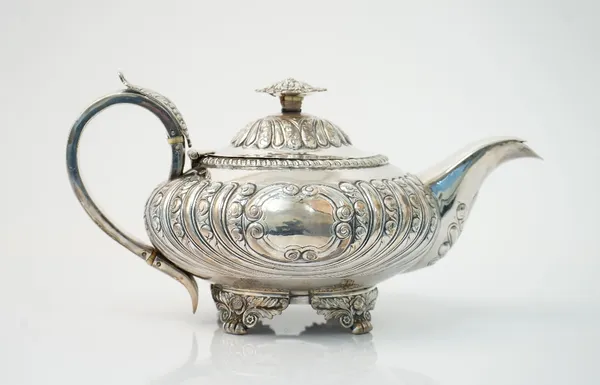 A George IV silver teapot, of compressed circular form, decorated with scroll and plain fluted bands, the hinged lid with a foliate finial and with a
