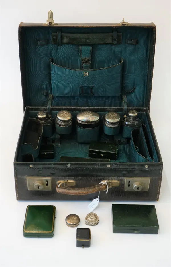 A late Victorian leather toilet case containing five silver topped faceted glass bottles and jars, the lids London 1899, another silver lid and a Vict