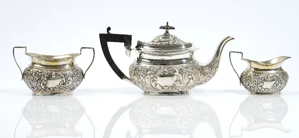 A late Victorian silver three piece tea set, comprising; a teapot having black fittings, a twin handled sugar bowl and a milk jug, each piece with flo