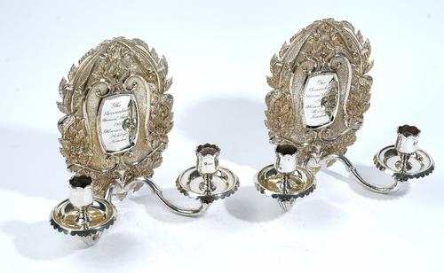 A pair of silver twin light candle wall sconces, the back plates of shaped oval form, decorated with tortoises, feathers and floral sprays, each twin