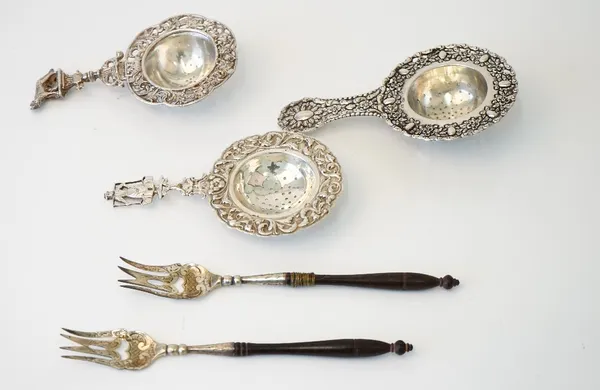 A Dutch tea strainer, decorated with a floral border, the handle finial modelled as a milkmaid, a tea strainer with a wolf finial, detailed 800, anoth