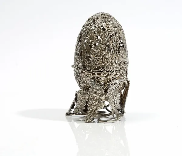 A silver model of a hinged egg enclosing a tiger, the exterior pierced with floral and foliate decoration, with a stand further decorated with floral