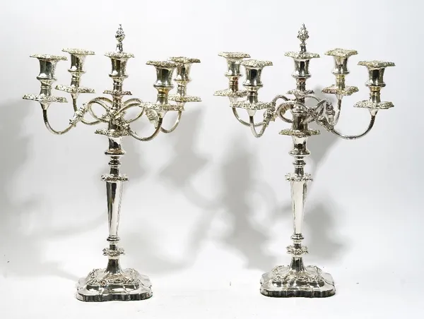 A pair of silver plated on copper five light table candelabra, with scrolling arms, decorated borders, the central light having a detachable flame fin