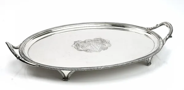 A George III silver oval twin handled tray, engraved with an armorial to the centre, within a boldly gadroon decorated rim, between foliate capped han