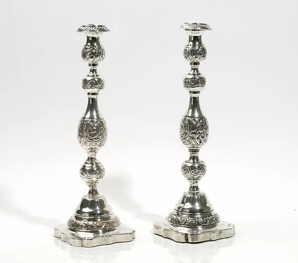 A pair of silver table candlesticks, each having a knopped bulbous stem with foliate scrolled decoration and raised on a shaped square foot, London 19