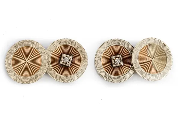 A pair of two colour gold and diamond dress cufflinks, each circular front mounted with a small cushion shaped diamond in a square surround, otherwise