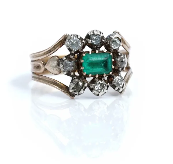 An early 19th century gold and silver set emerald and diamond cluster ring, mounted with the step cut emerald at the centre, in a surround of eight va