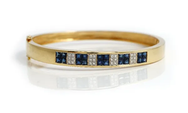 A French gold, sapphire and diamond set oval hinged bangle, the front mounted with five sapphire four stone clusters, mounted with square cut sapphire