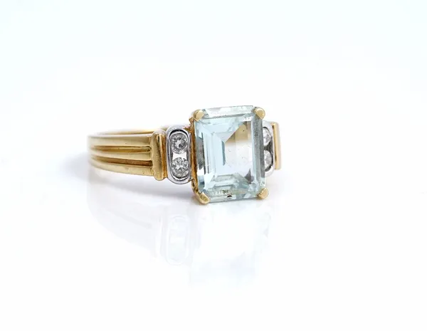 An 18ct two colour gold ring, claw set with a cut cornered rectangular step cut aquamarine, between two pairs of circular cut diamonds, between ridged