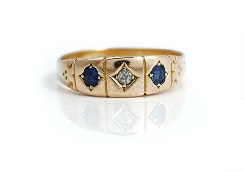 A 15ct gold, diamond and sapphire three stone ring, gypsy set with a cushion shaped diamond to the centre, between two cushion shaped sapphires, (no d