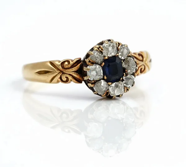 A gold, sapphire and diamond nine stone cluster ring, mounted with a step cut sapphire at the centre in a surround of eight cushion shaped diamonds, b