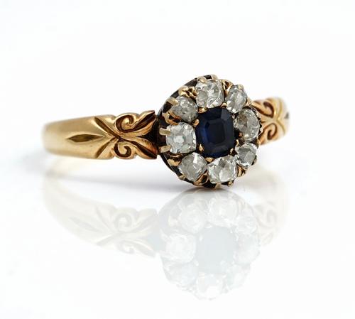 A gold, sapphire and diamond nine stone cluster ring, mounted with a step cut sapphire at the centre in a surround of eight cushion shaped diamonds, b