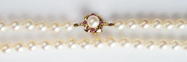 A single row necklace of uniform cultured pearls, on a gold, ruby and cultured pearl set clasp, detailed 14 K, length 41cm.