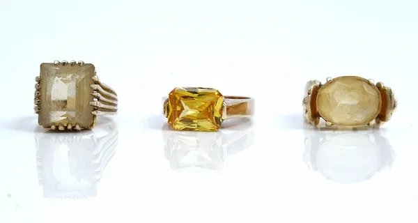 A 9ct gold ring, claw set with an oval cut citrine, a 9ct gold ring, claw set with a rectangular step cut citrine and a yellow gem set solitaire ring,