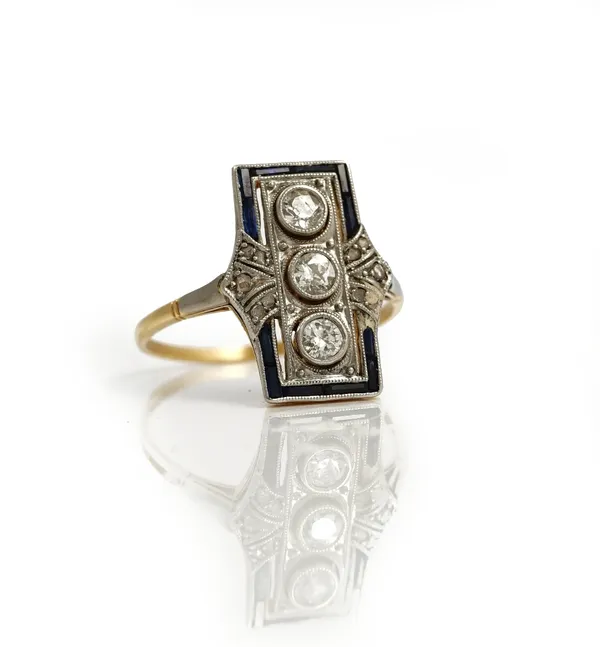 A platinum fronted gold, diamond and synthetic sapphire ring, in a panel shaped design, mounted with the three principal cushion shaped diamonds at th