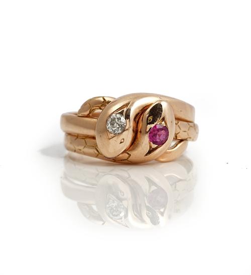 A gold, diamond and ruby ring, designed as two interwoven snakes, mounted with a cushion shaped diamond to one head and with a cushion shaped ruby to