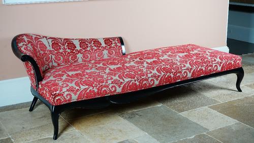 A large ebonised chaise longue, with shaped back and stuff-over seat, on cabriole legs, upholstered in green linen with raised red cut-floral design,