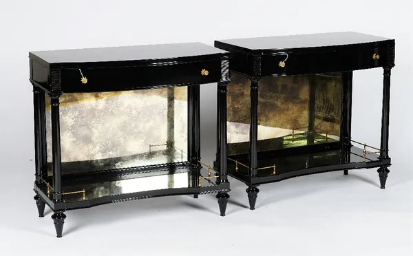 A pair of ebonised bowfronted console tables, in Empire style, with frieze drawers, mirrored backs and galleried undertiers, 77cm wide x 71cm high.