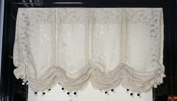 A pair of cream linen Roman blinds hung with black and white bobble tassels.142cm wide x 230cm long