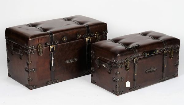 A graduated pair of chocolate brown leather trunks with button-down tops, the largest 83cm wide x 45cm high, the smallest 73cm x 37cm high, (2).