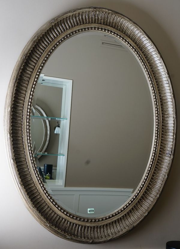 A George III style oval wall mirror, in grained fluted and ribbon tied moulded frame, 96cm wide x 124cm high.