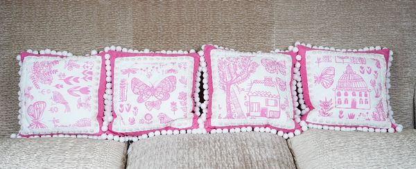 A set of four cushions, upholstered in pink linen the fronts printed with varying scenes bordered with white bobbles (4).