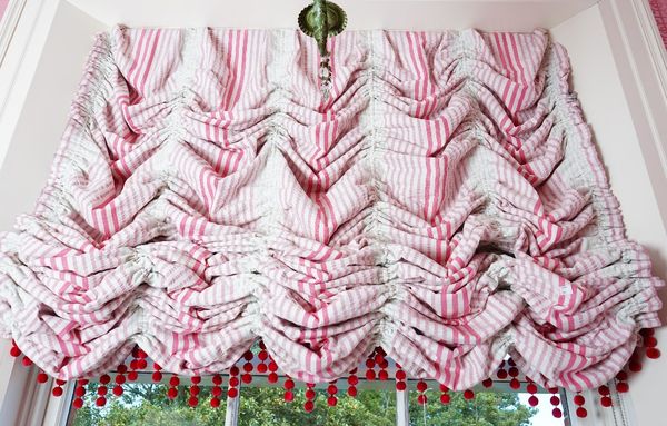 A Roman blind, in shades of pink interspaced by green bandings hung with bobbles, 130cm wide x 150cm high